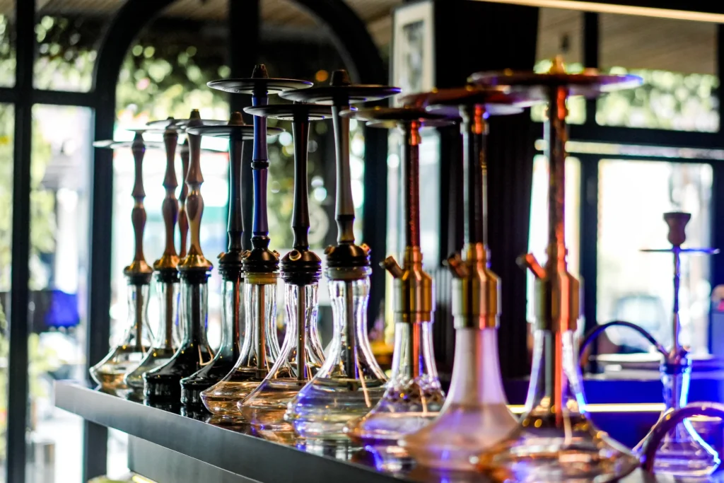 A beautiful lineup of various hookahs featuring different glass bases and stems resting on a sleek bar counter, showcasing the options you might see when choosing a hookah for beginner.