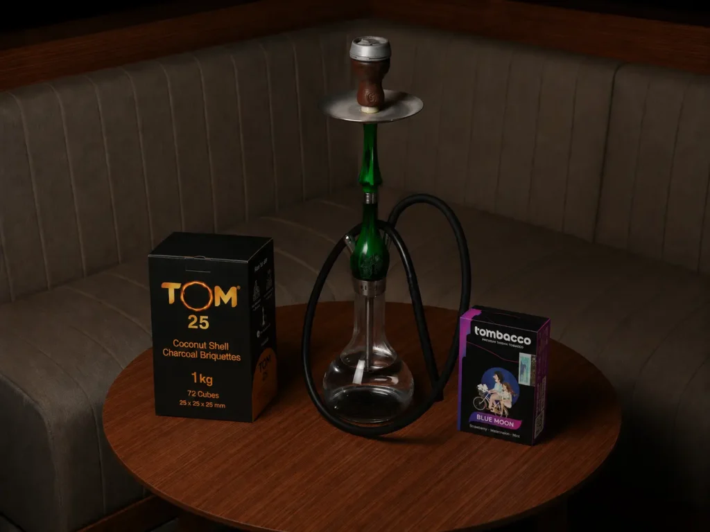 A complete setup resting on a wooden table featuring a green hookah, coconut shell charcoal briquettes, and Tombacco shisha, highlighting everything needed for a perfect hookah for beginner kit.